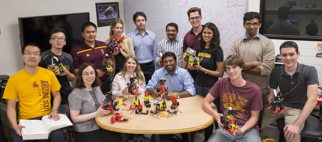 ACS Lab group photo from 2015. Multiple seated around a table full of small robots